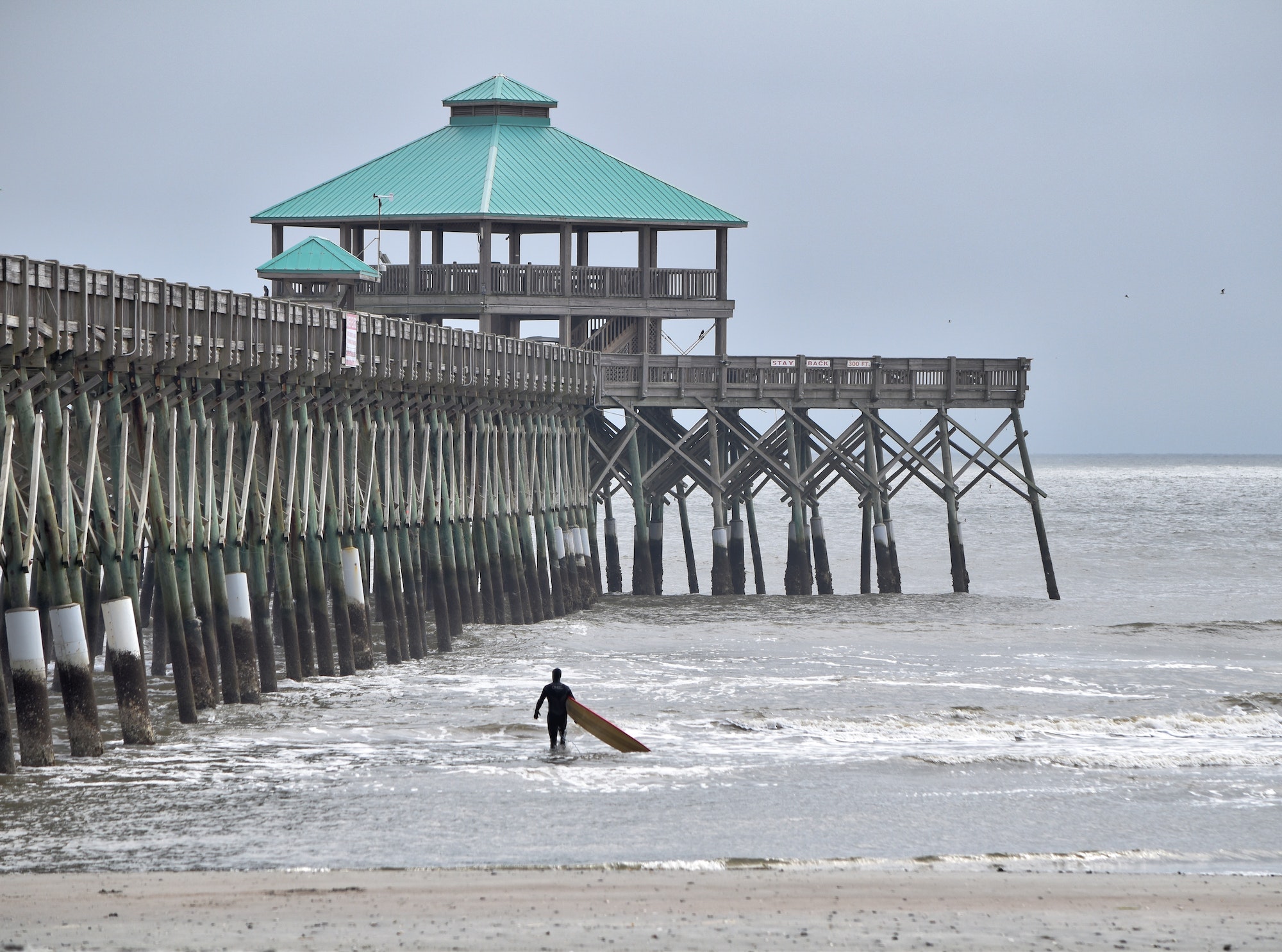 Beautiful background picture of a surfer by the pier in Charleston South Carolina entering the waves